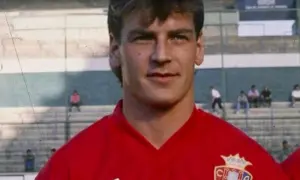 Jan Urban, piłkarz w czerwonej koszulce z herbem klubu, na tle trybun stadionu.