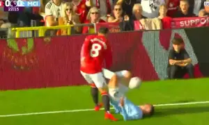 Piłkarz Manchesteru United w czerwonej koszulce z numerem 8 przewraca zawodnika Manchesteru City na murawę.