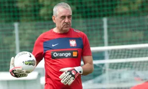 Jacek Kazimierski, trener bramkarzy, w czerwonej koszulce z orłem i logo Orange, trzyma piłkę i rękawice bramkarskie.
