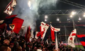 Tłum kibiców Genoa CFC z flagami na stadionie. Dym i światła tworzą atmosferę meczu.