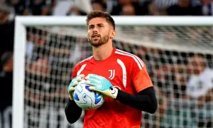 Bramkarz Juventusu w czerwonej koszulce trzyma piłkę w rękawicach.