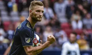 Piłkarz Kacper Przybyłko z piłką w ręku, świętuje zwycięstwo na boisku.