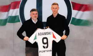 Rafał Adamski z numerem 9 na koszulce, obok niego mężczyzna, na tle flagi i logo klubu.