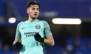 Piłkarz Jakub Moder w turkusowej koszulce Brighton & Hove Albion, z rękawiczkami na dłoniach, gotowy do gry.