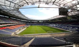 Pusta HDI Arena, stadion klubu Hannover 96, z zieloną murawą i rzędami niebieskich i czerwonych siedzeń pod przeszklonym dachem.