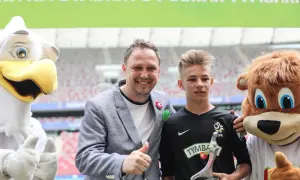 Paweł Kryszałowicz z młodym piłkarzem i maskotkami na stadionie.