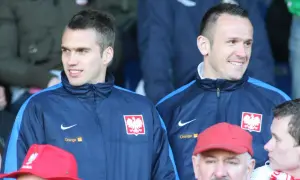 Dwóch piłkarzy w dresach reprezentacji Polski, jeden z nich to Łukasz Sosin, uśmiecha się do kibiców.
