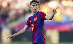 Młody gavi pilkarz FC Barcelony w akcji, z wyrazem skupienia na twarzy i uniesionym palcem wskazującym.