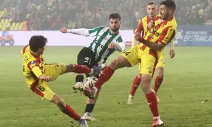Zacięta walka o piłkę w meczu Korona Kielce – Zagłębie Lubin. Piłkarze w żółto-czerwonych strojach walczą z zawodnikiem w zielono-białej koszulce.