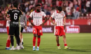 Piłkarze Girona FC po trudnych rozgrywkach. Zawodnicy w czerwono-białych strojach stoją na boisku, wyraźnie zmęczeni.
