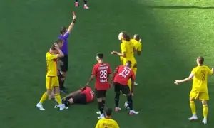 Sędzia pokazuje czerwoną kartkę w trakcie meczu Stade Rennais. Piłkarz leży na boisku, inni zawodnicy reagują.