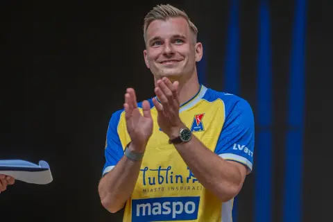 Uśmiechnięty Mateusz Legowski w żółto-niebieskiej koszulce z logo Motor Lublin klaszcze, świętując sukces.