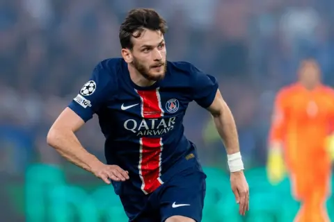 Piłkarz PSG w ciemnoniebieskiej koszulce z czerwonymi pasami, gotowy do akcji. Chwicza Kwaracchelia w akcji.
