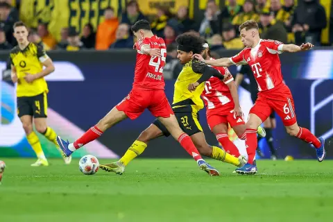 Piłkarze w czerwonych strojach walczą o piłkę na boisku podczas meczu **Bundesliga: rozgrywki**.