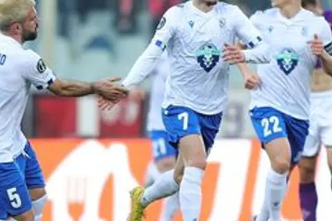 Piłkarze Lecha Poznań w białych strojach, jeden z numerem 5, gratulują sobie po meczu z Fiorentiną.