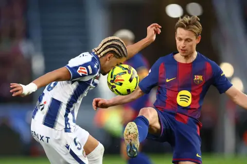 Piłkarze walczą o piłkę. Jeden z nich, Frenkie de Jong, w niebiesko-czerwonym stroju, wydaje się być w trakcie akcji, która mogła doprowadzić do jego kontuzji.