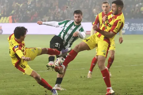 Zacięta walka o piłkę w meczu Korona Kielce – Zagłębie Lubin. Piłkarze w żółto-czerwonych strojach walczą z zawodnikiem w zielono-białej koszulce.