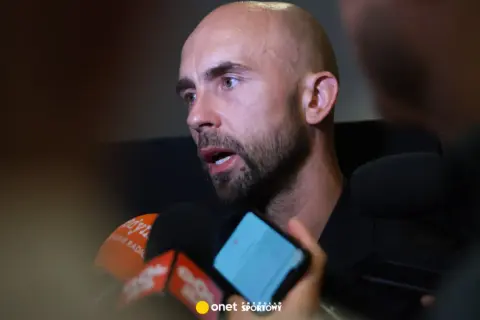 Adrian Mierzejewski udziela wywiadu dziennikarzom, odpowiadając na pytania przed mikrofonami.