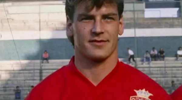 Jan Urban, piłkarz w czerwonej koszulce z herbem klubu, na tle trybun stadionu.