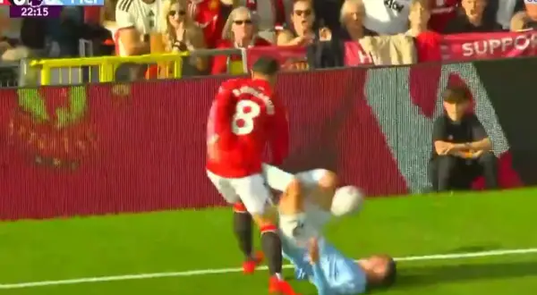 Piłkarz Manchesteru United w czerwonej koszulce z numerem 8 przewraca zawodnika Manchesteru City na murawę.