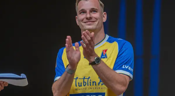 Uśmiechnięty Mateusz Legowski w żółto-niebieskiej koszulce z logo Motor Lublin klaszcze, świętując sukces.