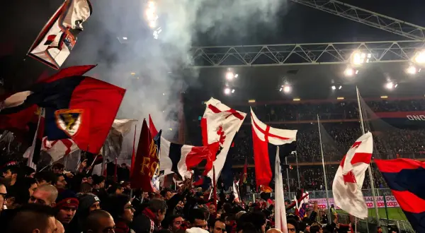 Tłum kibiców Genoa CFC z flagami na stadionie. Dym i światła tworzą atmosferę meczu.