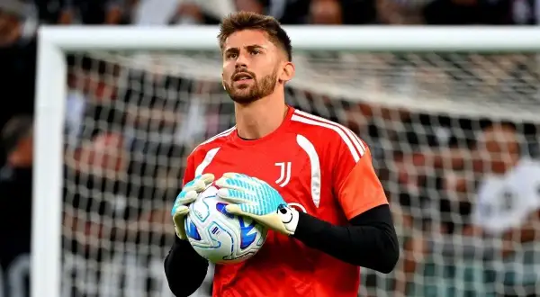 Bramkarz Juventusu w czerwonej koszulce trzyma piłkę w rękawicach.