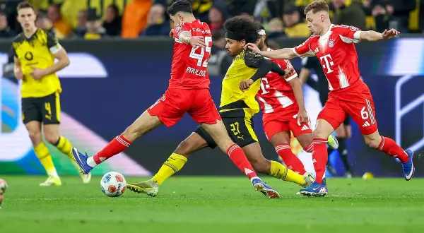 Piłkarze w czerwonych strojach walczą o piłkę na boisku podczas meczu **Bundesliga: rozgrywki**.