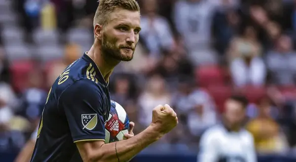 Piłkarz Kacper Przybyłko z piłką w ręku, świętuje zwycięstwo na boisku.