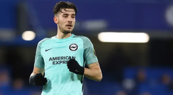 Piłkarz Jakub Moder w turkusowej koszulce Brighton & Hove Albion, z rękawiczkami na dłoniach, gotowy do gry.