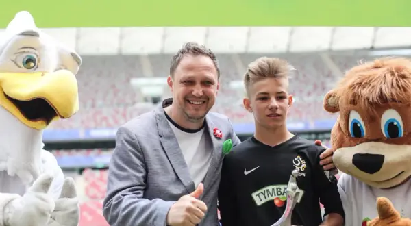 Paweł Kryszałowicz z młodym piłkarzem i maskotkami na stadionie.