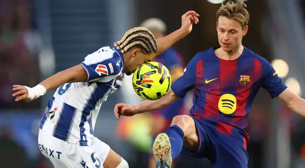Piłkarze walczą o piłkę. Jeden z nich, Frenkie de Jong, w niebiesko-czerwonym stroju, wydaje się być w trakcie akcji, która mogła doprowadzić do jego kontuzji.