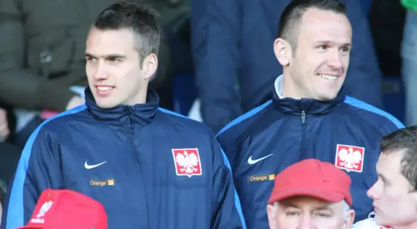 Dwóch piłkarzy w dresach reprezentacji Polski, jeden z nich to Łukasz Sosin, uśmiecha się do kibiców.