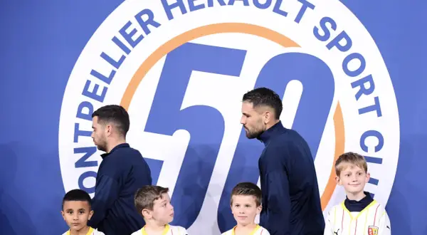 Piłkarze Montpellier HSC, klubu z ligi francuskiej, pozują z młodymi kibicami przed banerem z okazji 50-lecia klubu.
