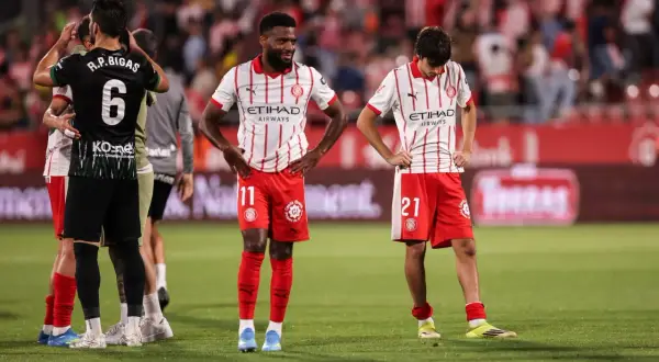 Piłkarze Girona FC po trudnych rozgrywkach. Zawodnicy w czerwono-białych strojach stoją na boisku, wyraźnie zmęczeni.