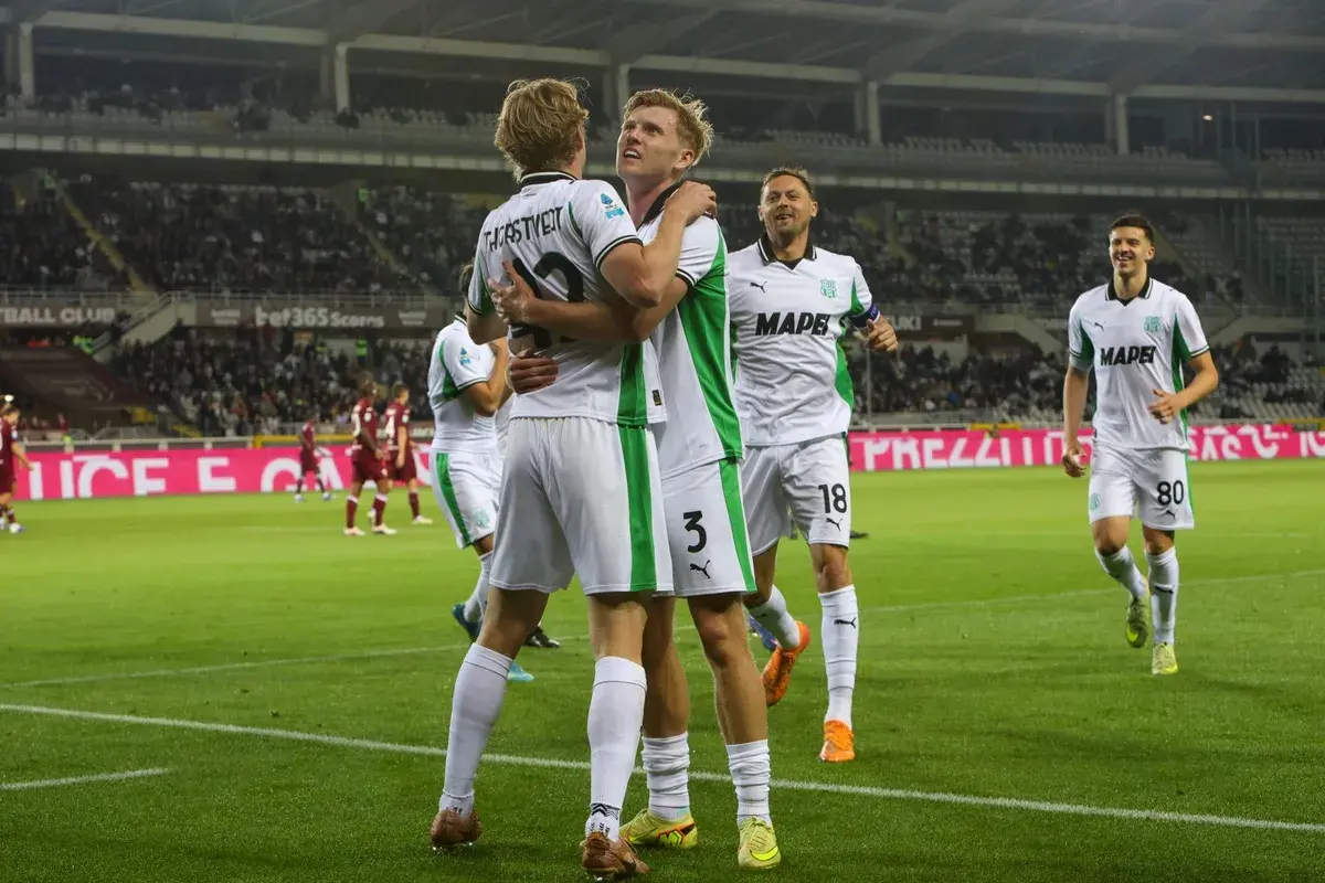 Piłkarze Sassuolo świętują bramkę podczas rozgrywek. Dwóch zawodników przytula się na boisku, podczas gdy inni cieszą się z sukcesu.