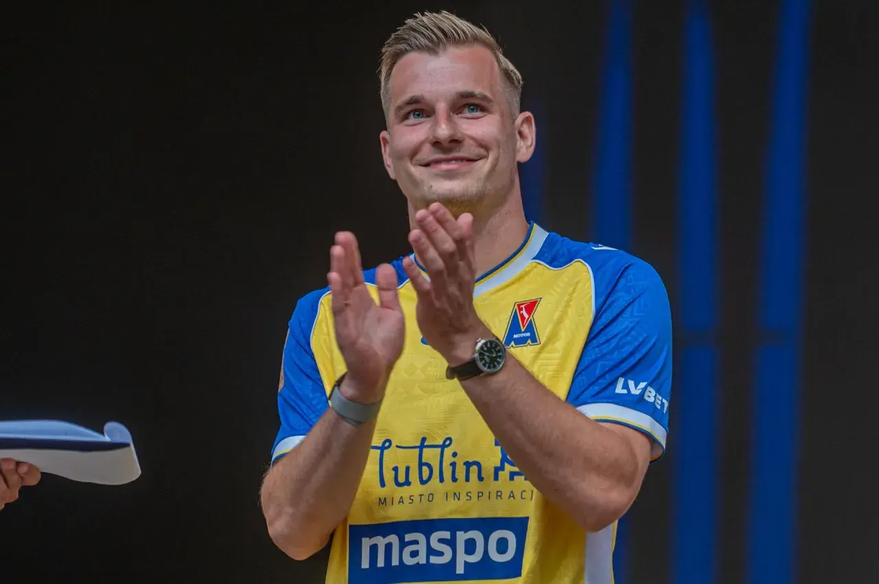 Uśmiechnięty Mateusz Legowski w żółto-niebieskiej koszulce z logo Motor Lublin klaszcze, świętując sukces.