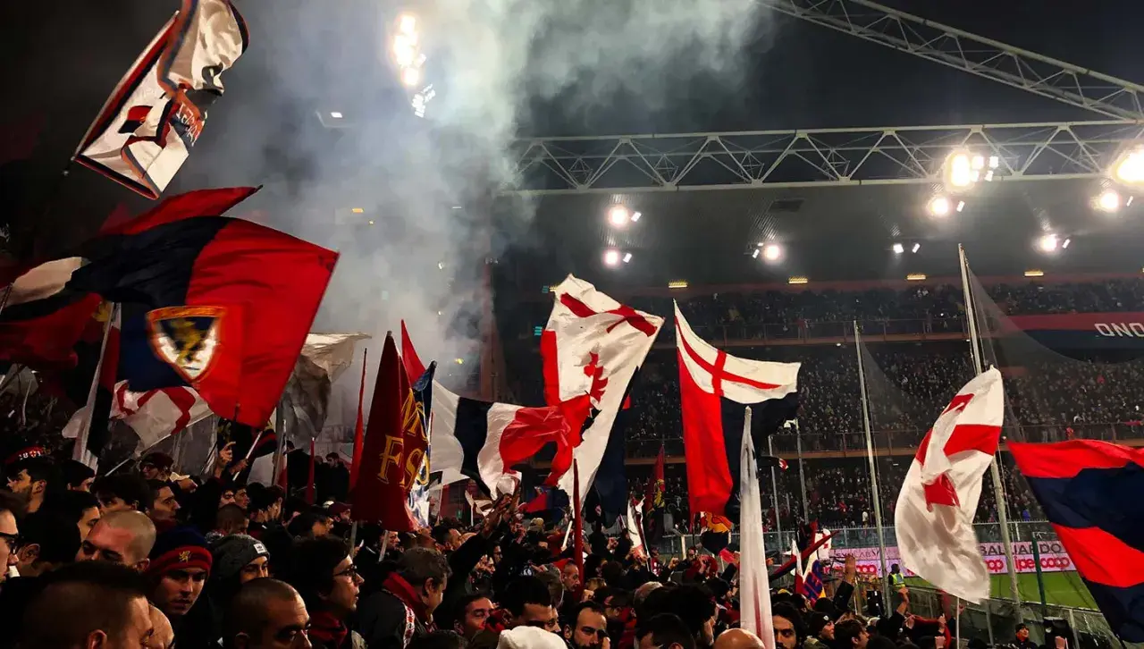 Tłum kibiców Genoa CFC z flagami na stadionie. Dym i światła tworzą atmosferę meczu.
