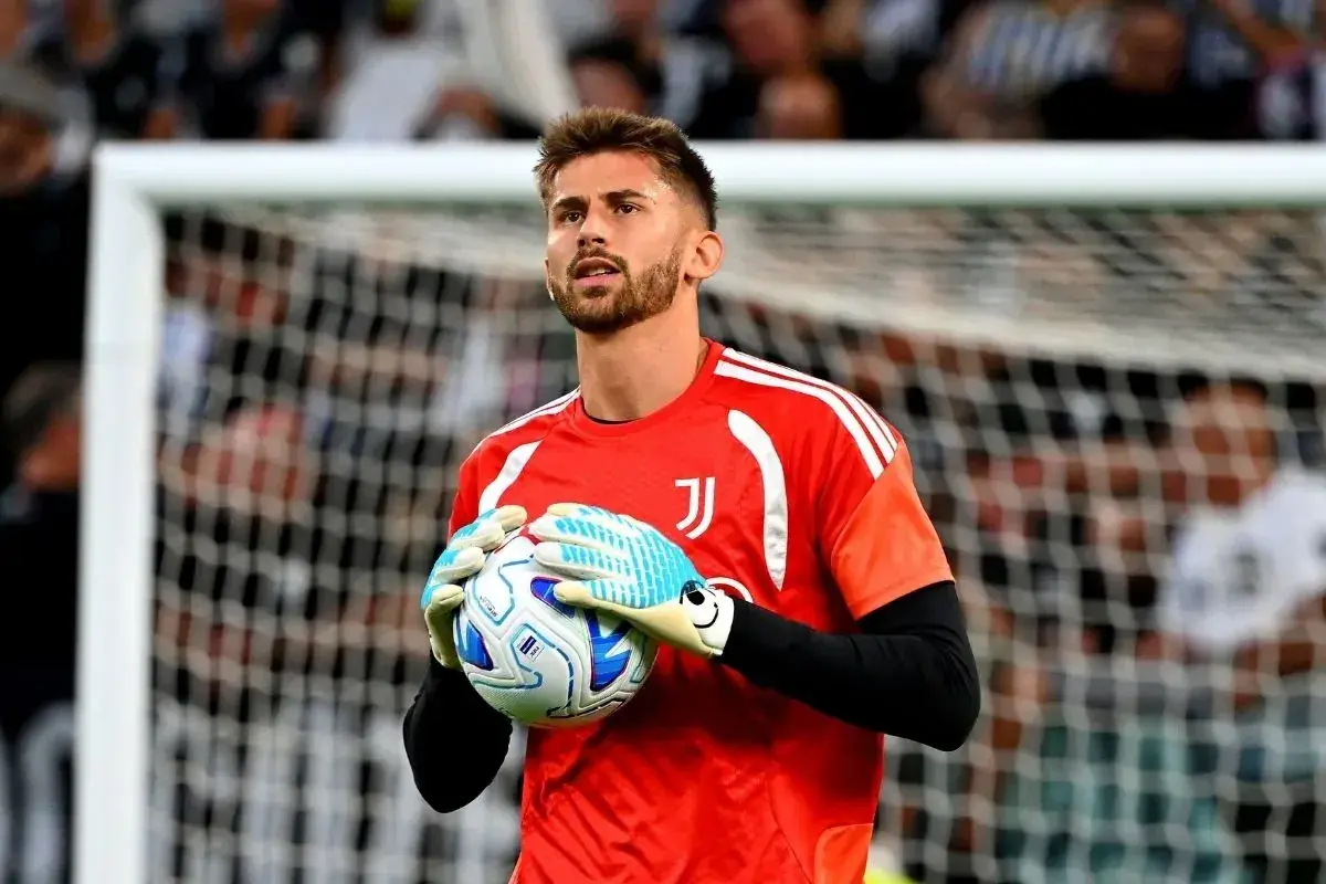 Bramkarz Juventusu w czerwonej koszulce trzyma piłkę w rękawicach.