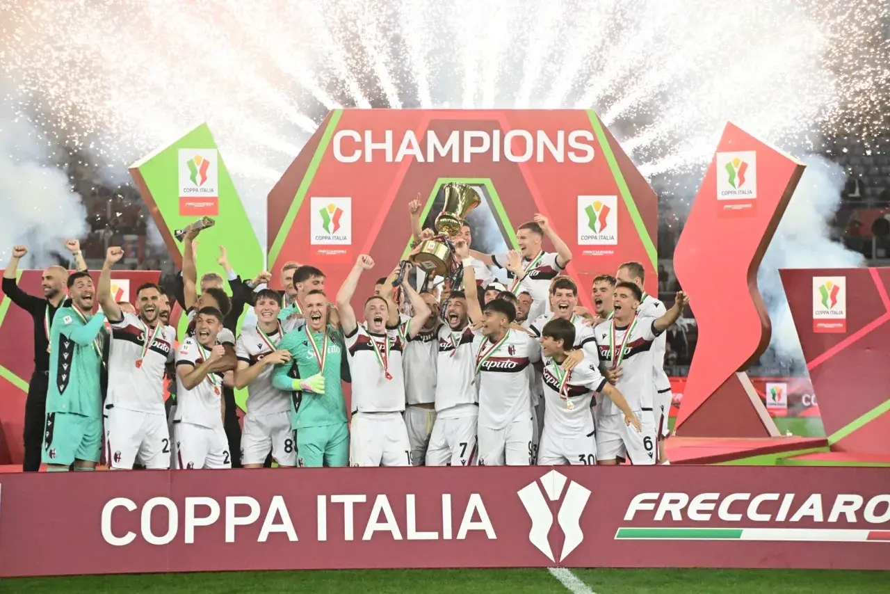 Bologna FC świętuje zwycięstwo w rozgrywkach Coppa Italia, wznosząc puchar na tle fajerwerków i napisu "CHAMPIONS".