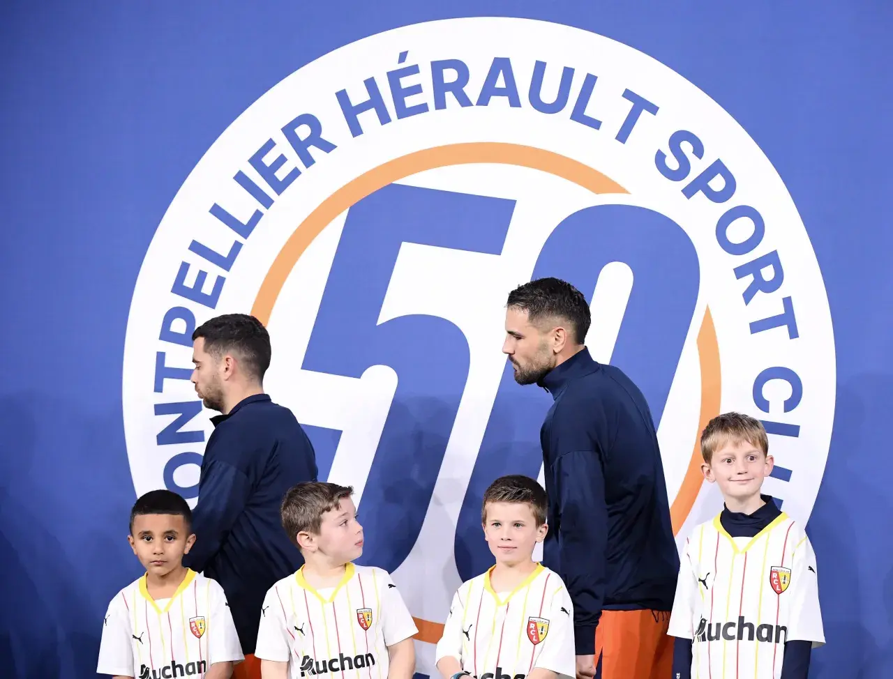 Piłkarze Montpellier HSC, klubu z ligi francuskiej, pozują z młodymi kibicami przed banerem z okazji 50-lecia klubu.