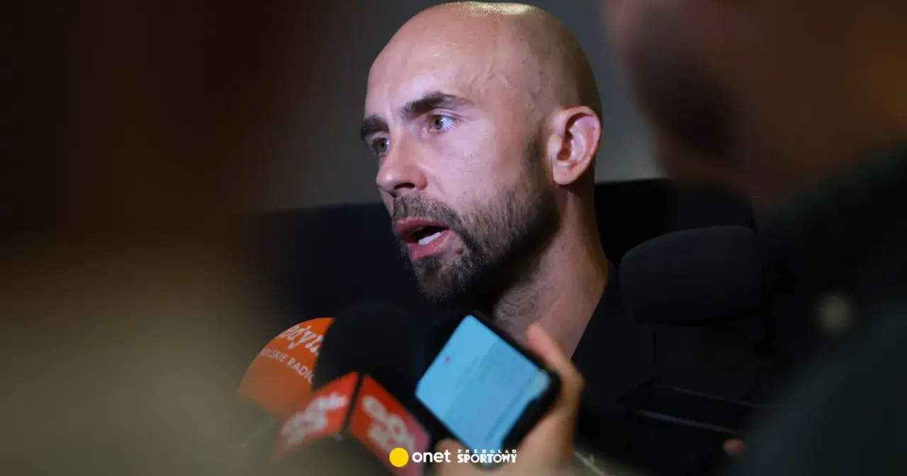 Adrian Mierzejewski udziela wywiadu dziennikarzom, odpowiadając na pytania przed mikrofonami.