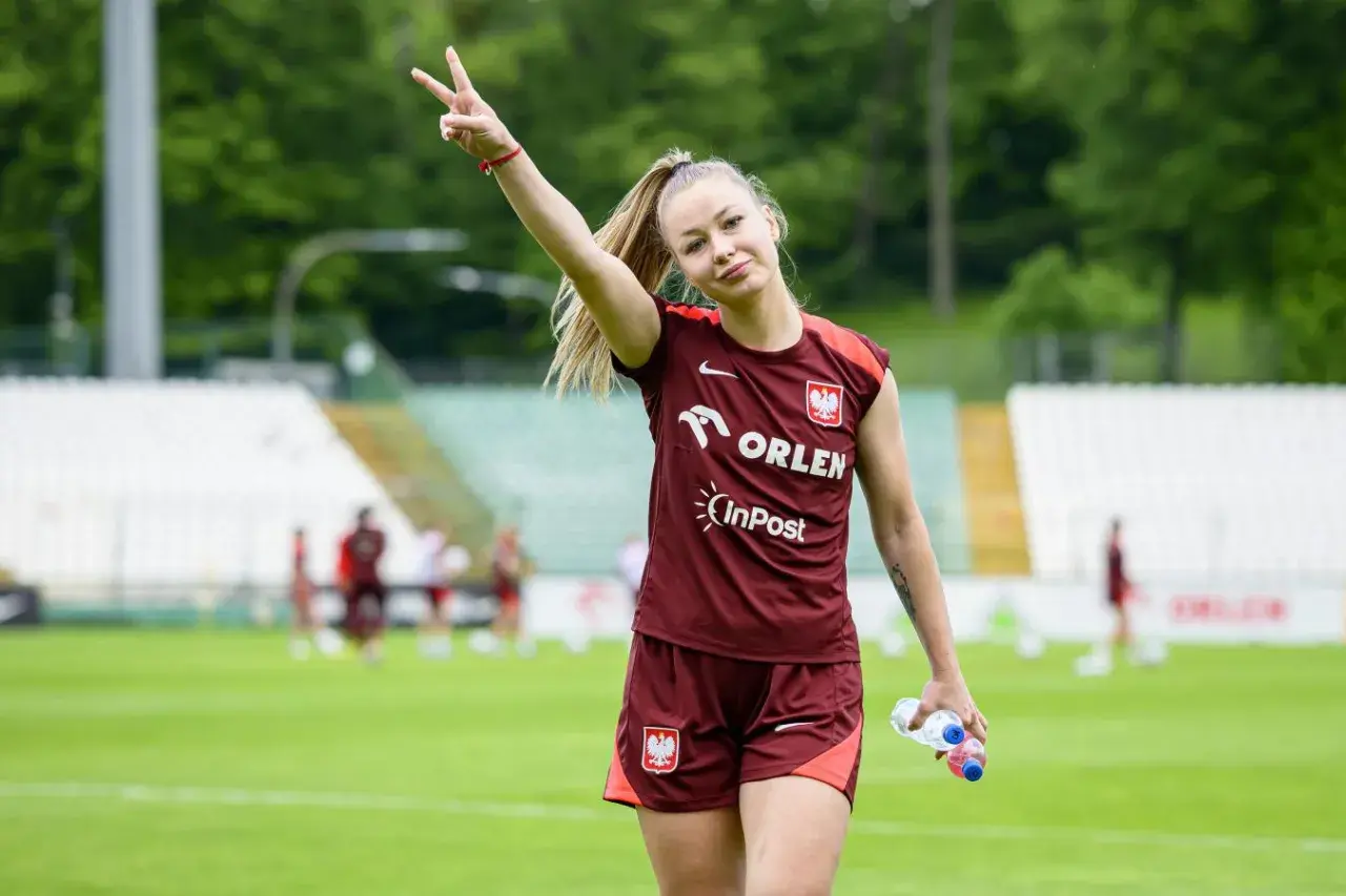 Weronika Zawistowska w dresie reprezentacji Polski, z butelką wody w dłoni, pokazuje znak pokoju.
