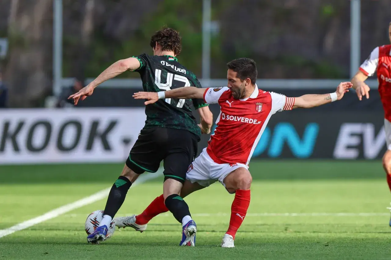 Piłkarze w akcji podczas rozgrywek SC Braga. Jeden w czerwonej koszulce, drugi w zielonej.
