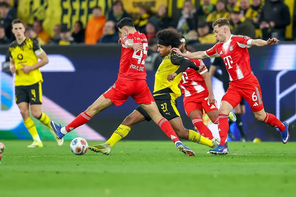 Piłkarze w czerwonych strojach walczą o piłkę na boisku podczas meczu **Bundesliga: rozgrywki**.