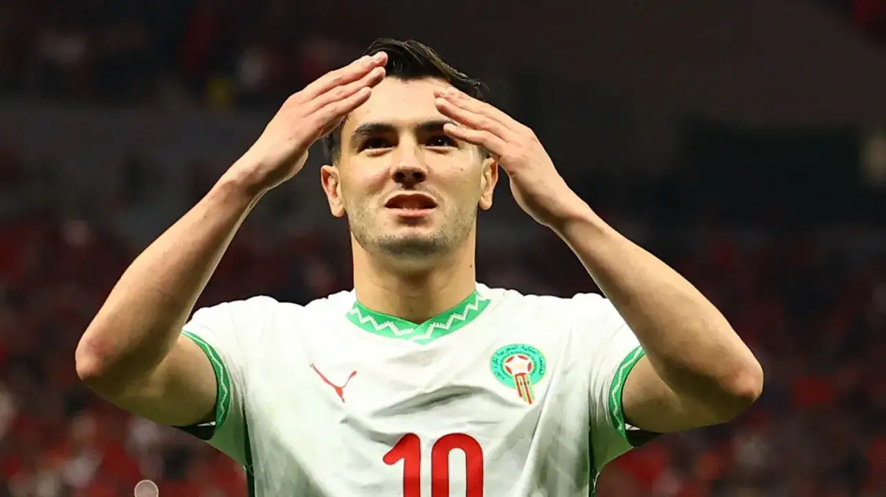 Piłkarz Brahim Diaz w białej koszulce z numerem 10 i zielonym kołnierzykiem, pozdrawia kibiców.