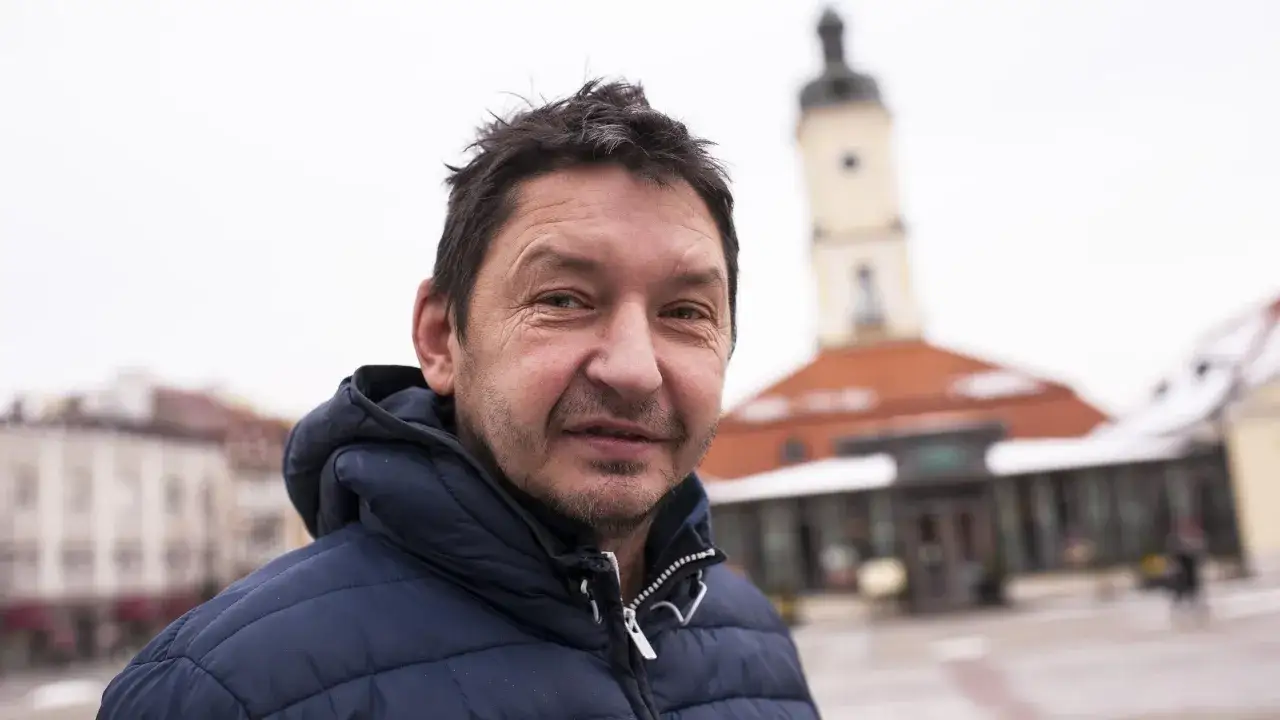 Dariusz Czykier w ciemnej kurtce na tle miejskiego placu z wieżą.