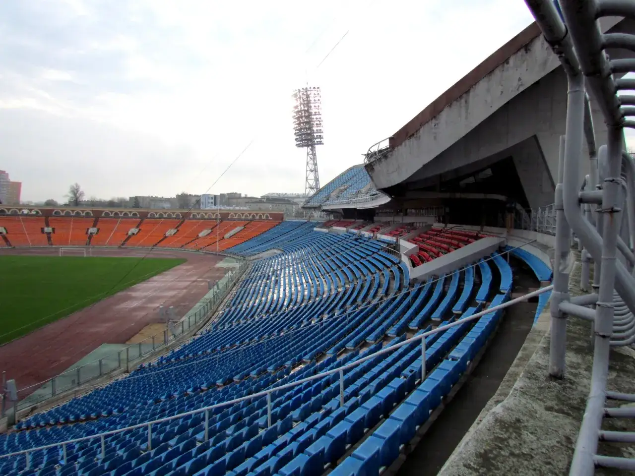 Puste trybuny stadionu Dynamo Mińsk, z niebieskimi i pomarańczowymi siedzeniami, czekają na kibiców.