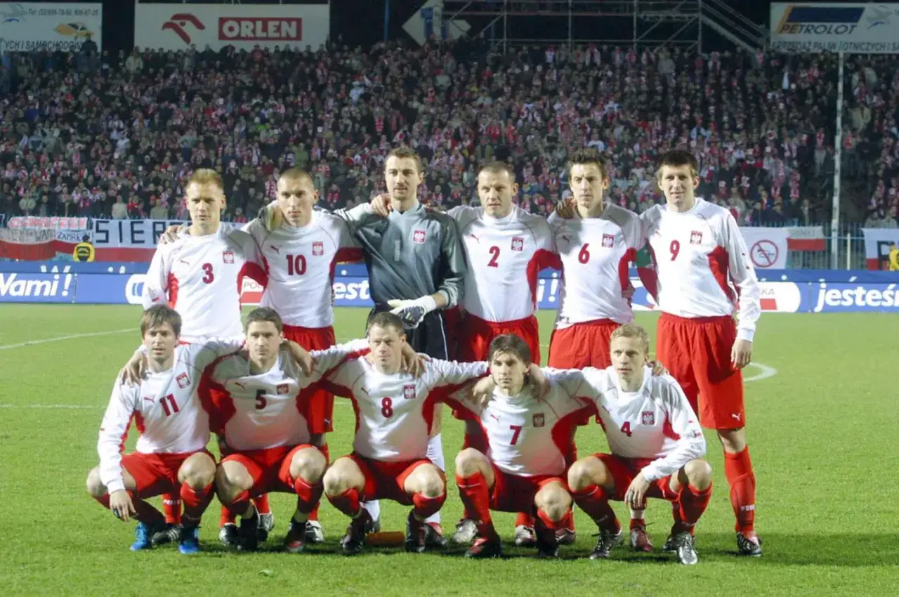 Reprezentacja Polski w piłce nożnej przed meczem Polska - USA. Piłkarze w białych strojach z czerwonymi elementami pozują do zdjęcia na tle trybun.