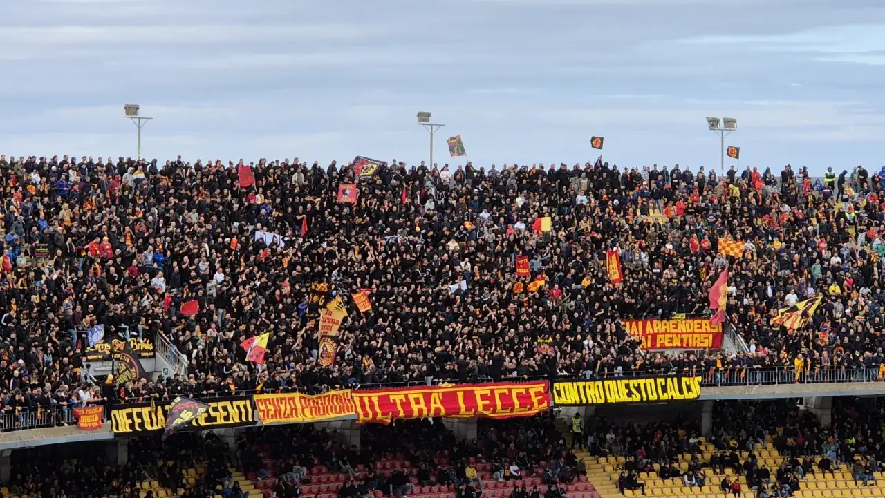 Tysiące kibic&oacute;w US Lecce w czarnych koszulkach, z flagami i transparentami, tworzą gorącą atmosferę na stadionie.